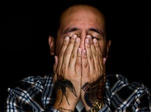 person with hands over eyes and tattoos on hands