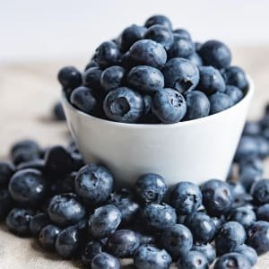 white bowl of blueberries with blueberries also around bottom of bowl