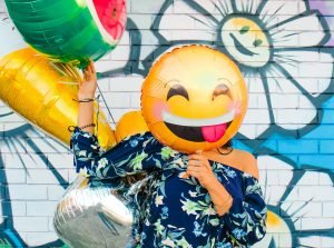 person with smiley face balloon covering natural face