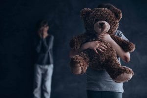 two children, one with stuffed toy and one in background with hands over eyes