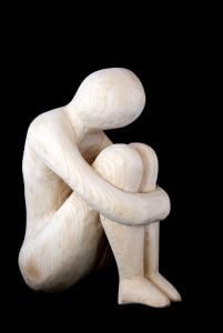 wooden figurine sitting while hugging knees to chest